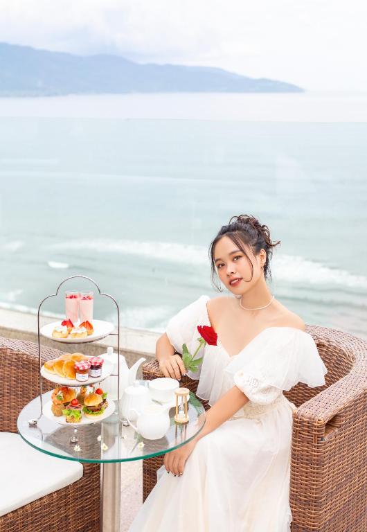 A sea-view afternoon-tea setting with pastries, sandwiches and tea on a wicker terrace.
