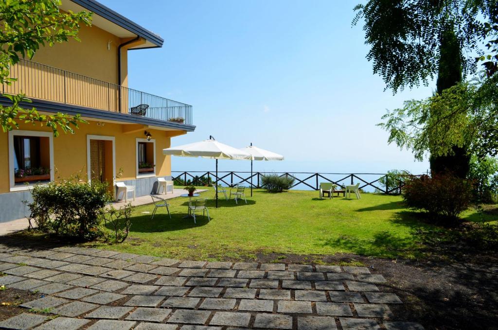 a house with a lawn with tables and umbrellas at L'Infinito Agriturismo - Rooms & Breakfast in SantʼAlfio
