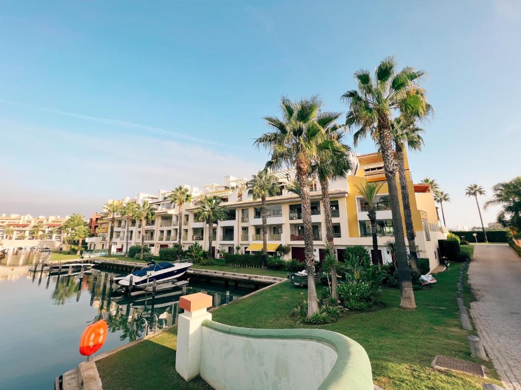 a large building with palm trees next to a body of water at Sotogrande Alboaire- Waterfront luxury 4 bedroom Apt in the Marina of Sotogrande in Sotogrande