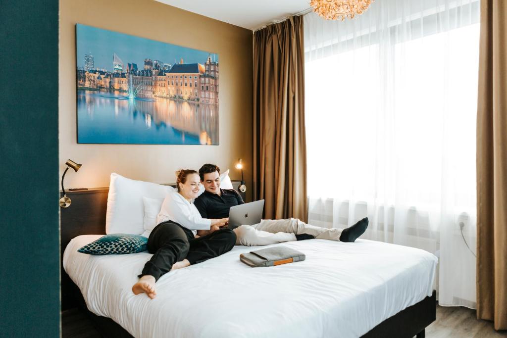 a man and woman sitting on a bed with a laptop at The Hague Teleport Hotel - Free Parking in The Hague