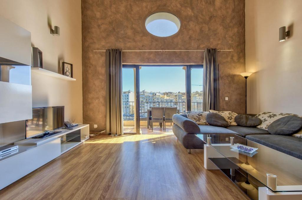 een woonkamer met een bank en een groot raam bij Spinola Court - Stunning Seaview Apartment & Penthouse on Spinola Bay by ShortletsMalta in St Julian's