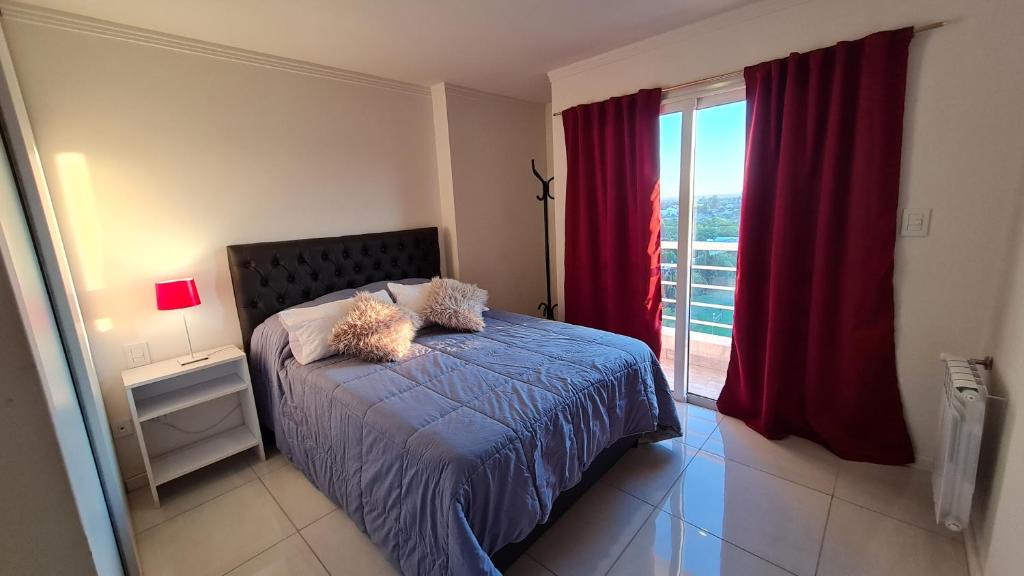 een slaapkamer met een bed en een raam met rode gordijnen bij Confort Río Cuarto I in Río Cuarto