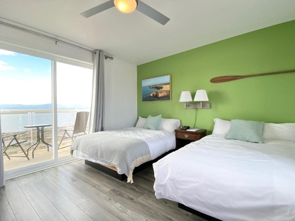 two beds in a room with a view of the ocean at La Plage Motel in Berthier-sur-Mer