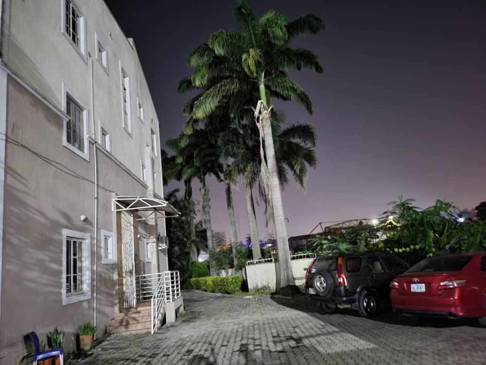 een palmboom en twee auto's geparkeerd naast een gebouw bij Chez B&D Suites and Apartments in Abuja