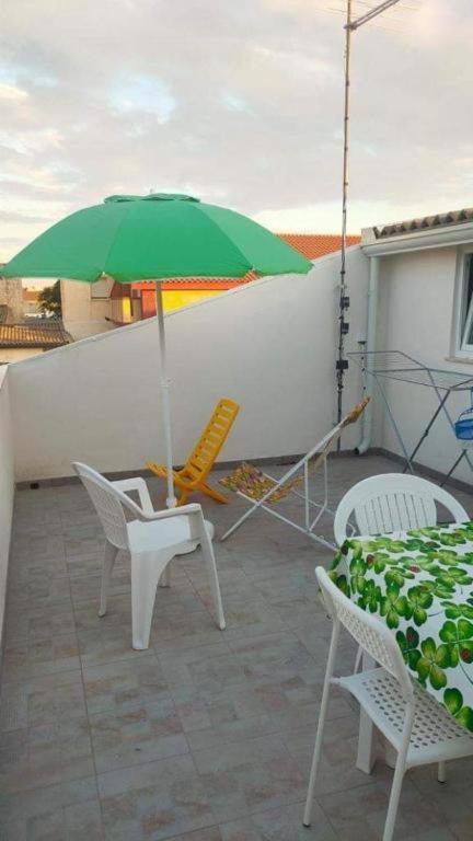 un ombrellone e sedie verdi su un patio di Appartamento sul mare Scoglitti 2 a Scoglitti