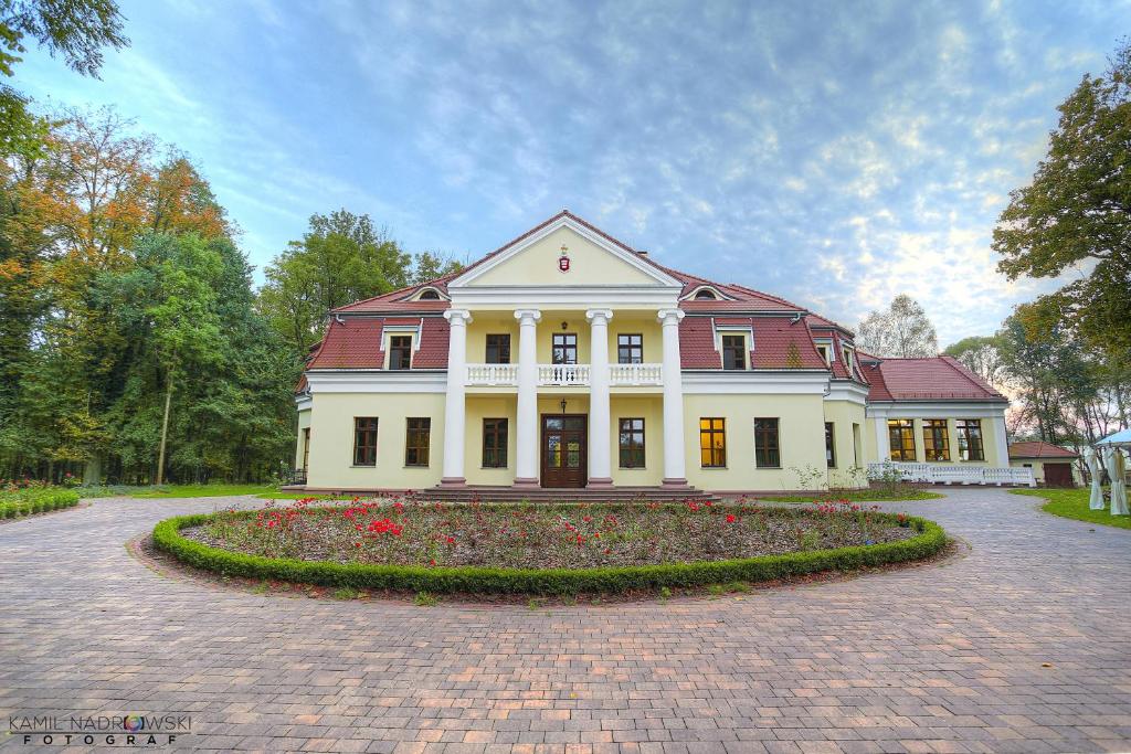 una gran casa blanca con una zona de flores delante de ella en Dwór Słupia en Zarzecze