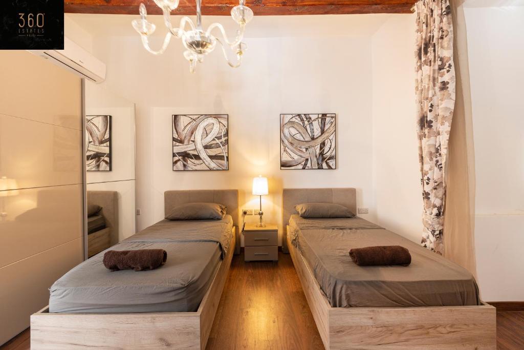 two beds in a room with a chandelier at Palazzo 16th Century Mdina, opposite St Paul's Cathedral by 360 Estates in Mdina