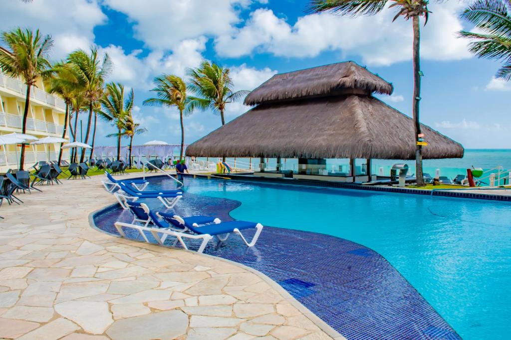 a swimming pool with chairs and palm trees and the ocean at Aram Natal Mar Hotel in Natal