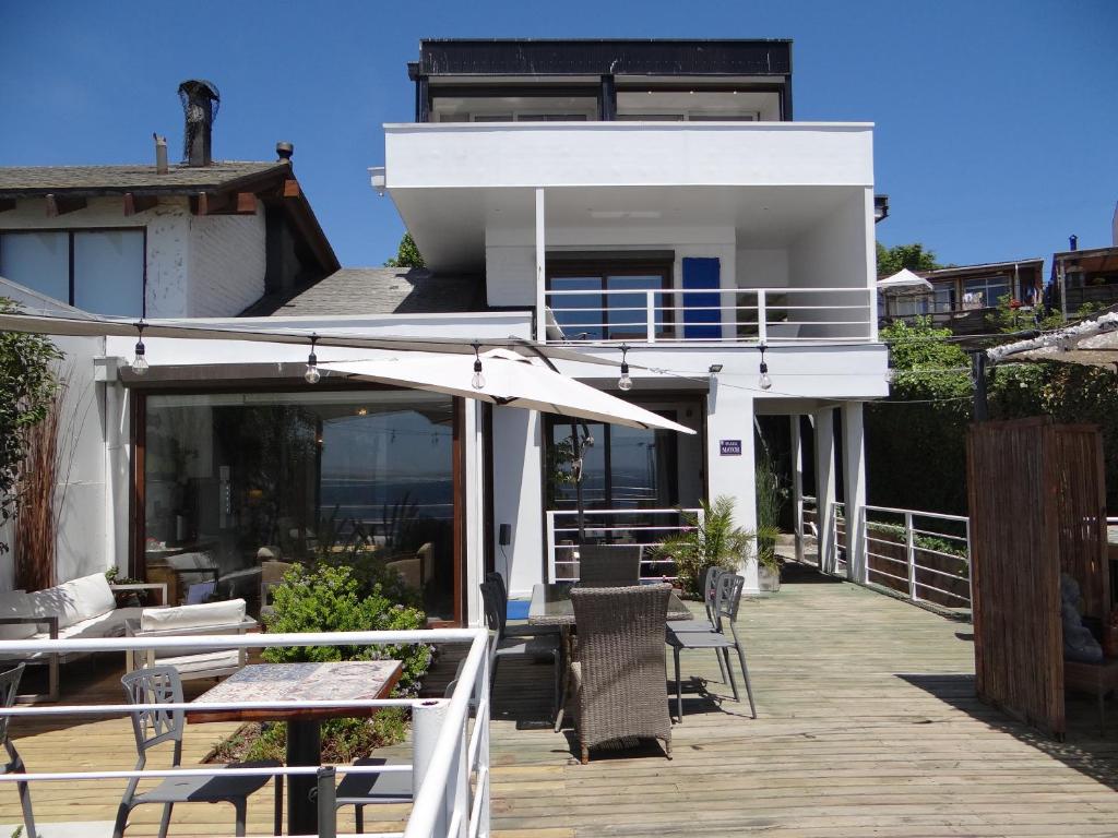 Casa blanca con terraza con sillas y sombrilla en Laura del Mar Hotel Boutique, en Concón