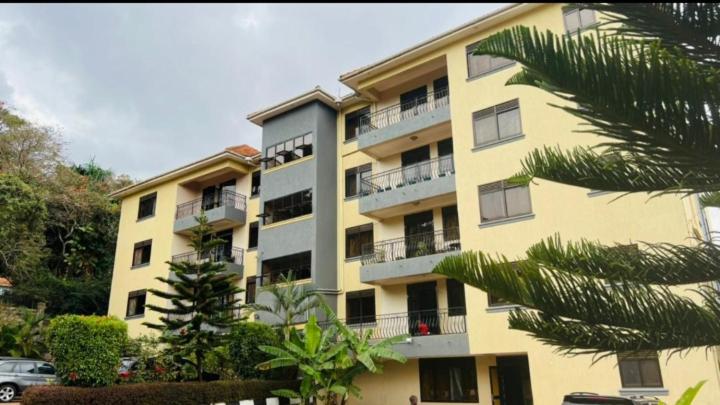 a yellow apartment building with balconies and a palm tree at PALATINE APARTMENTS MAKINDYE KIZUNGU, KAMPALA in Kampala