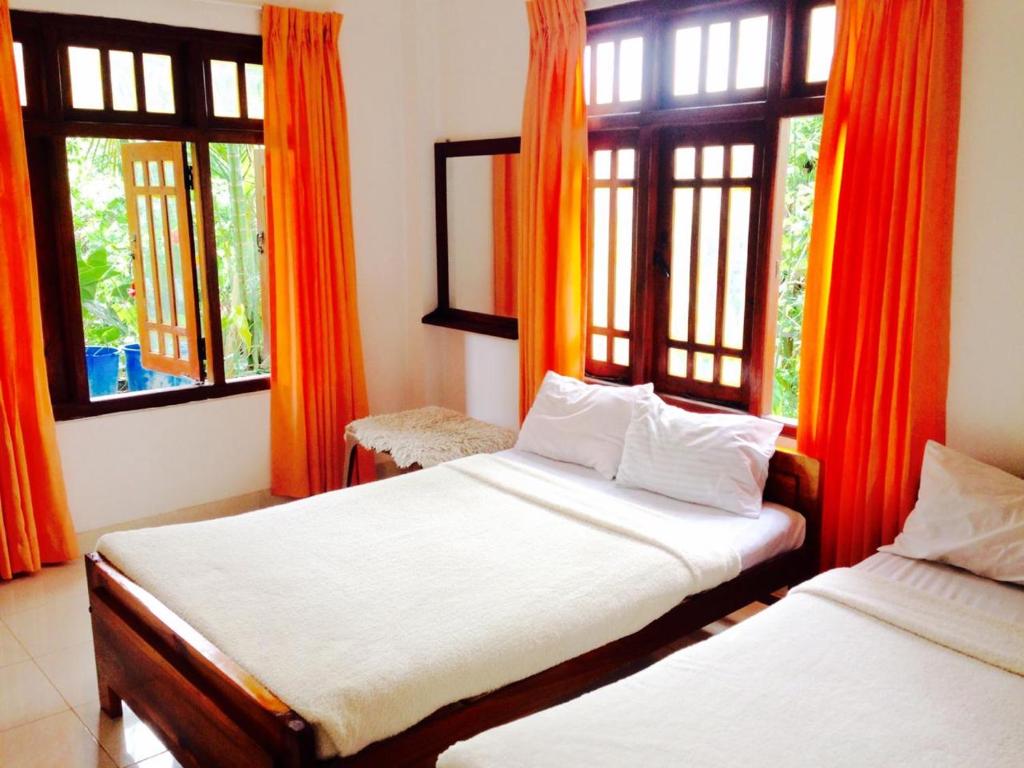 two beds in a room with orange curtains and windows at Cool Breeze guest inn in Bandarawela