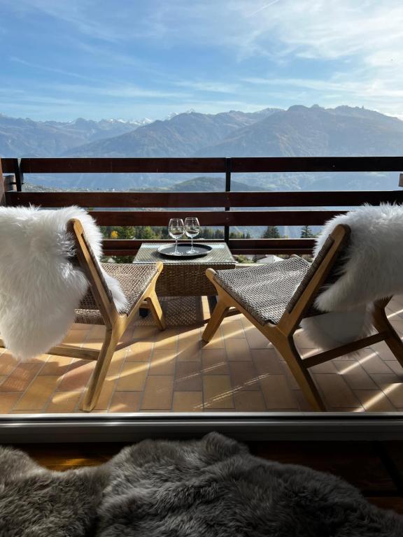 a balcony with two chairs and a table with wine glasses at Superbe studio Anzère, rénové, au pied des pistes in Anzère