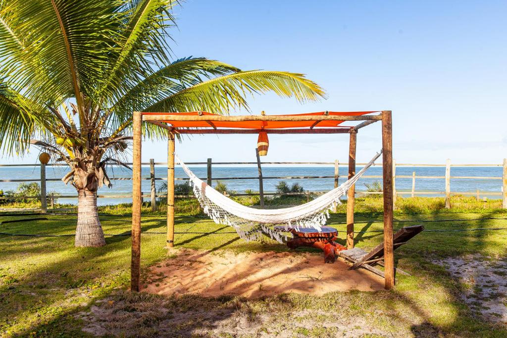 a hammock on a beach with a palm tree and the ocean at Pousada Vila Rosa - Caraiva in Caraíva