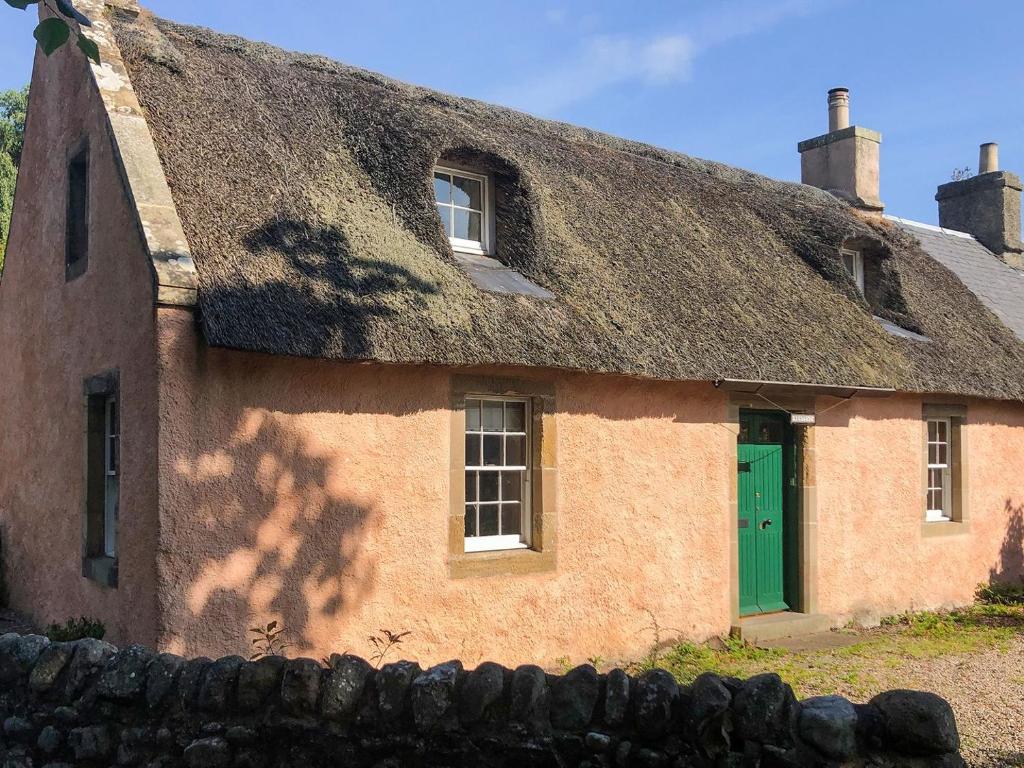 stary dom z dachem krytym strzechą i zielonymi drzwiami w obiekcie The Thatched Cottage w mieście St Andrews