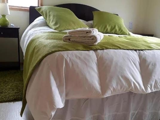 Una cama blanca con almohadas verdes y toallas. en Cabañas Frange en Puerto Natales