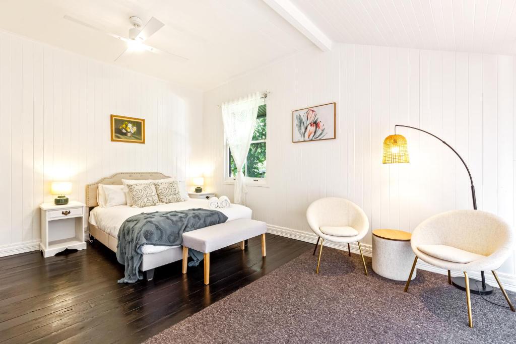 a white bedroom with a bed and two chairs at Unwind at Secret Garden Maleny 3 BR Family Home in Maleny