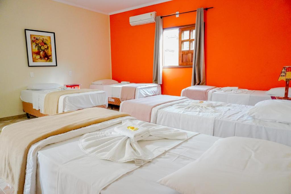 Habitación con camas blancas en una habitación con paredes de color naranja. en Pousada Kabana de Pedra, en Ibicoara