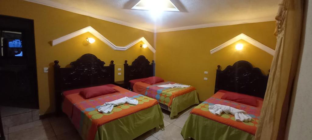 three beds in a room with yellow walls at Hotel Tinamit in San Pedro La Laguna