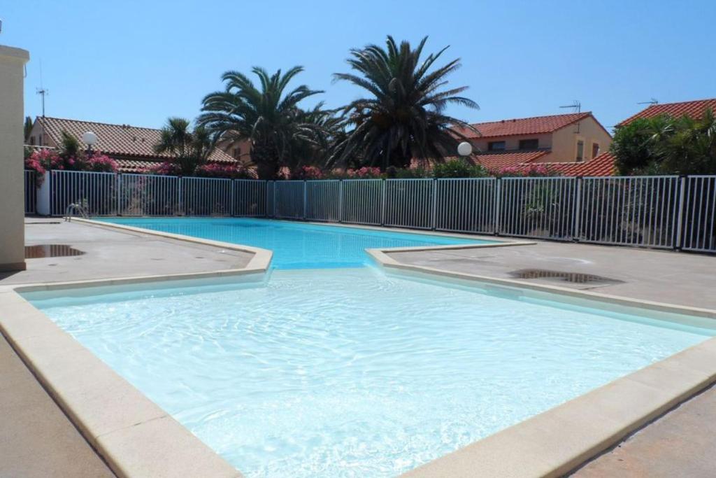 une grande piscine bleue avec une clôture et des palmiers dans l'établissement Villa 6p climatisée proche mer piscine equipements nautique, au Barcarès