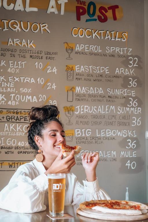 a woman sitting at a table eating a slice of pizza at The Post Hostel Jerusalem in Jerusalem