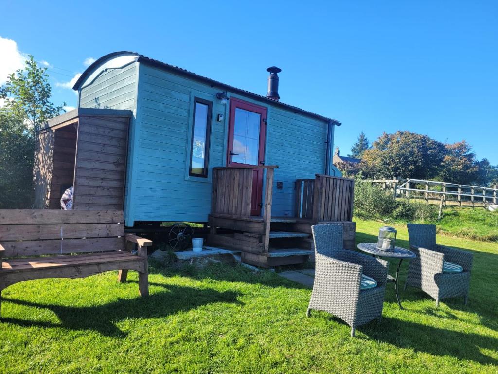 a blue tiny house with a bench and chairs at The Shepherds Hut at Forestview Farm in Greenisland