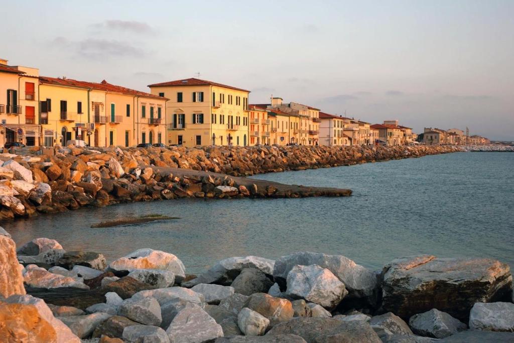 un groupe de bâtiments à côté de l'eau avec des rochers dans l'établissement Affreschi sul mare, à Marina di Pisa