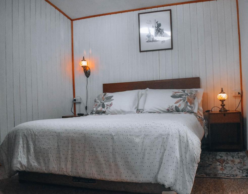 1 dormitorio con 1 cama con colcha blanca y 2 lámparas en Cabaña El Quijote, en Valdivia
