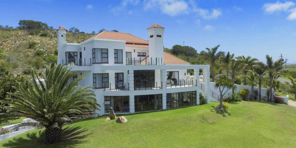 a large white house on top of a lush green field at Fly Me To The Moon Guesthouse in Mossel Bay