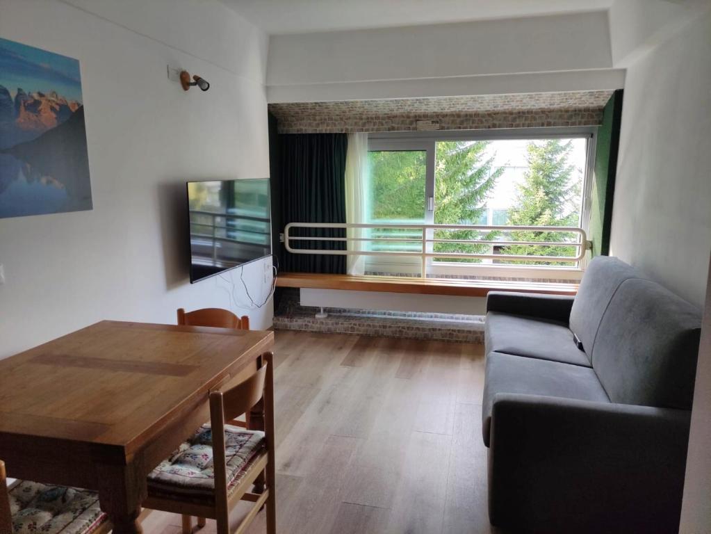 uma sala de estar com um sofá, uma mesa e uma janela em Genziana Apartment - CIPAT 22114 em Marilleva
