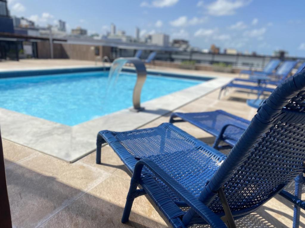 una piscina con sillas azules junto a una piscina en MARINAS PRAIA Flat - Cabo Branco by PenareiaTurBr, en João Pessoa