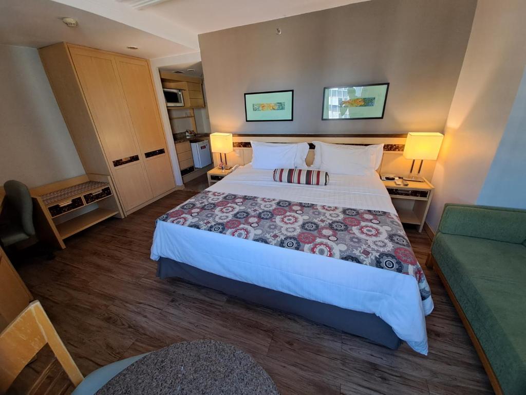 um quarto de hotel com uma cama grande e um sofá verde em Flat particular no Lets Idea Brasília em Brasília