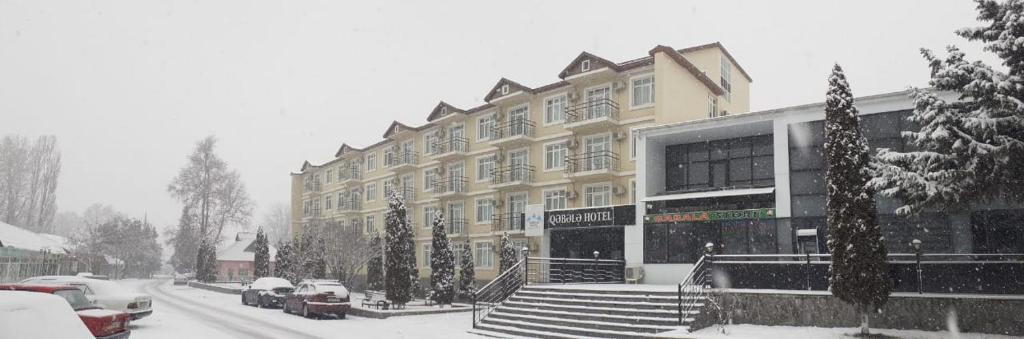un edificio cubierto de nieve con coches aparcados delante de él en Gabala Hotel en Daşca