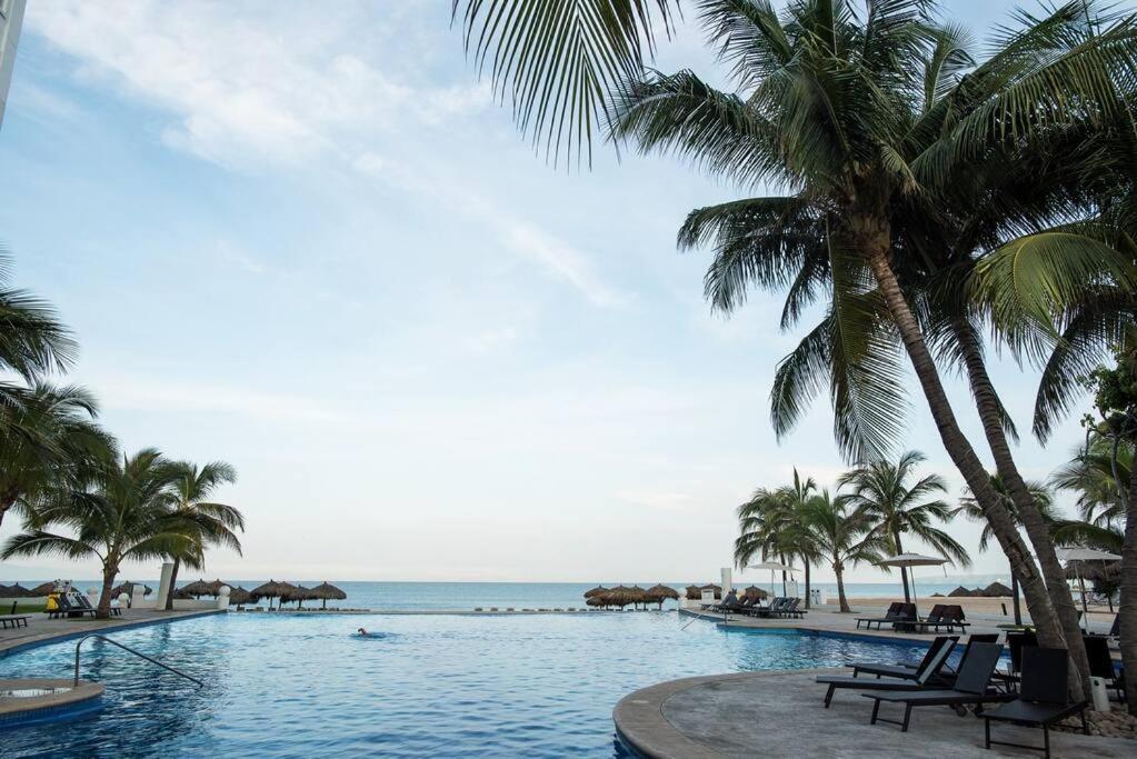 a swimming pool with palm trees and the beach at Villa Magna departamento en Nuevo Vallarta in Nuevo Vallarta