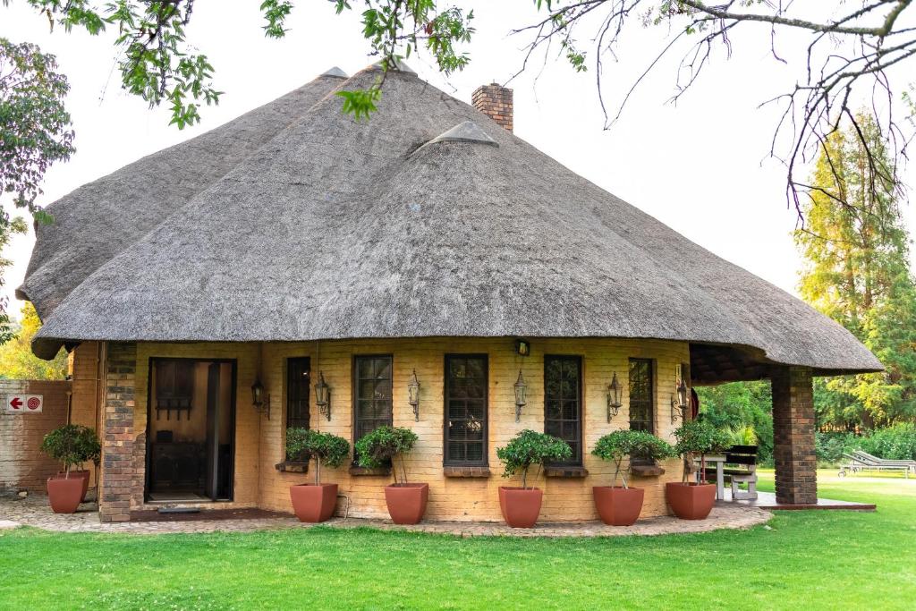 uma casa com telhado de palha com vasos de plantas em Hotel Nomad Belvedere Lodge em Midrand