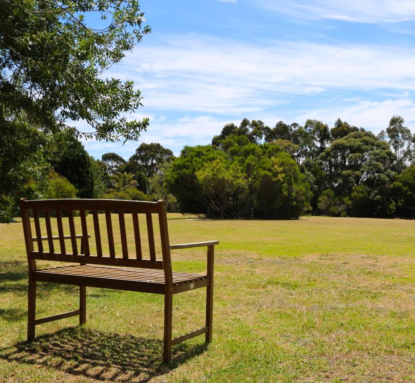 a wooden park bench sitting in a field at Bells Beach Cottages - Pet friendly cottage with wood heater in Torquay