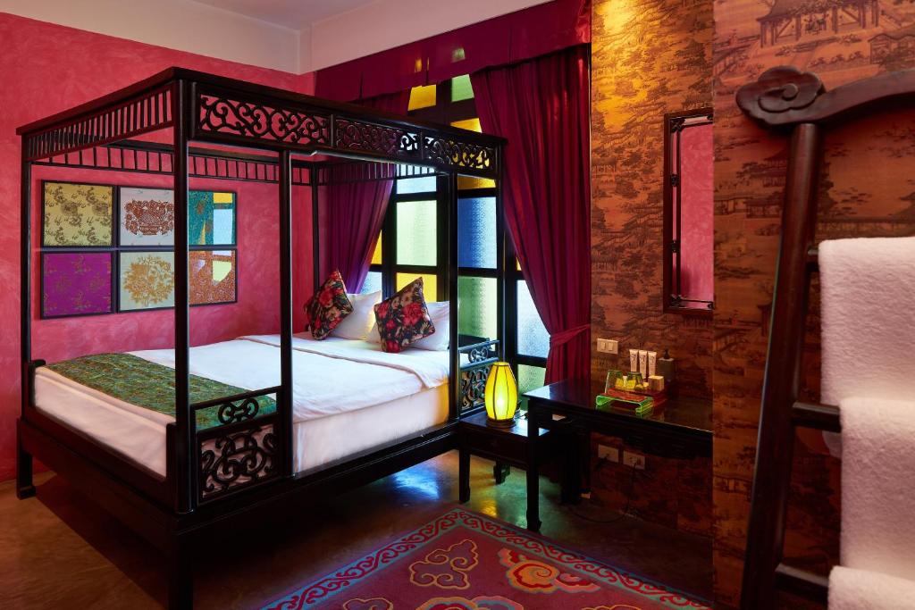 An ornate canopy bed sits beside stained-glass-style windows in a vivid red boutique bedroom.