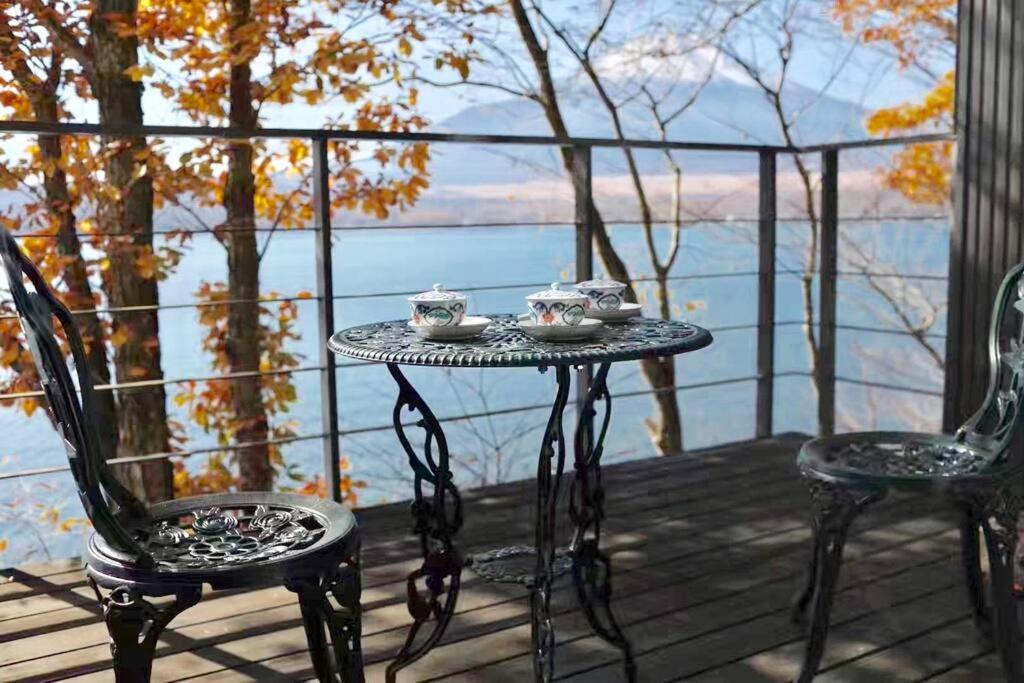 山中湖村にあるAway From Noise,View Fuji Mt In The Designer Houseのテーブルと椅子が備わるデッキから水辺の景色を望めます。