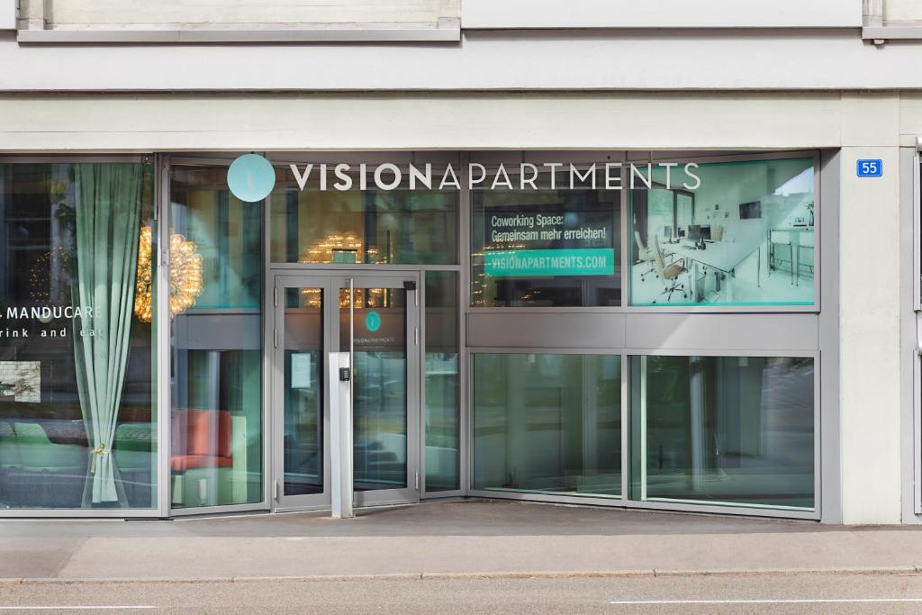 VISIONAPARTMENTS Basel Nauenstrasse - contactless check-in في بازل: مبنى زجاجي به لوحه مكتوب عليها اقسام الرؤيه