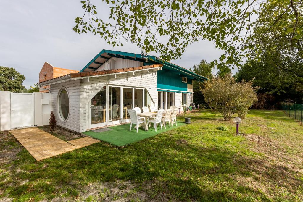 een klein wit huis met een terras en stoelen bij Villa bleue in Sanguinet