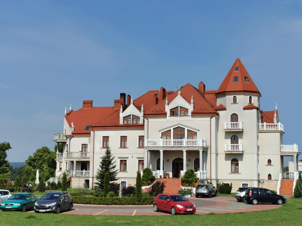 une grande maison blanche avec des voitures garées dans un parking dans l'établissement Pałac Koronny Noclegi & Wypoczynek, à Wodzisław