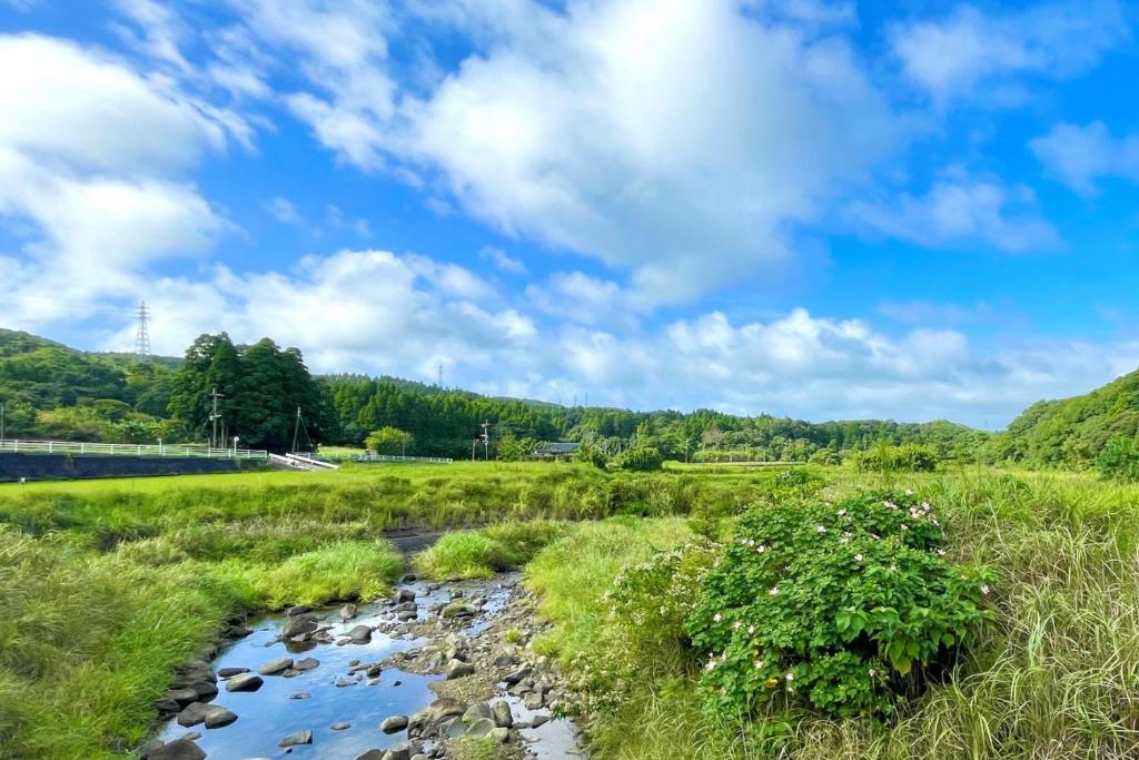 a stream in a field with a blue sky and clouds at Seiryukyou in Nishinoomote