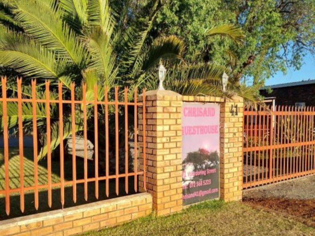 einen Zaun mit einem Schild vor einer Palme in der Unterkunft Chrisand Guesthouse in Kuruman