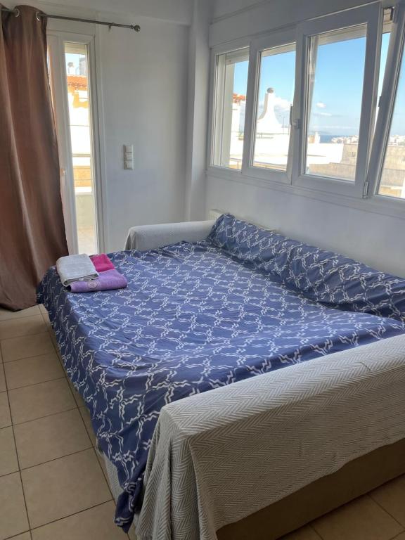 a bed with a blue comforter in a room with windows at Christos in Rafina