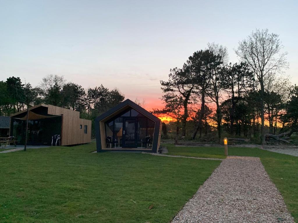 a small glass house with a sunset in the background at Tiny House in het groen, aan zee met privé Hottub in Callantsoog