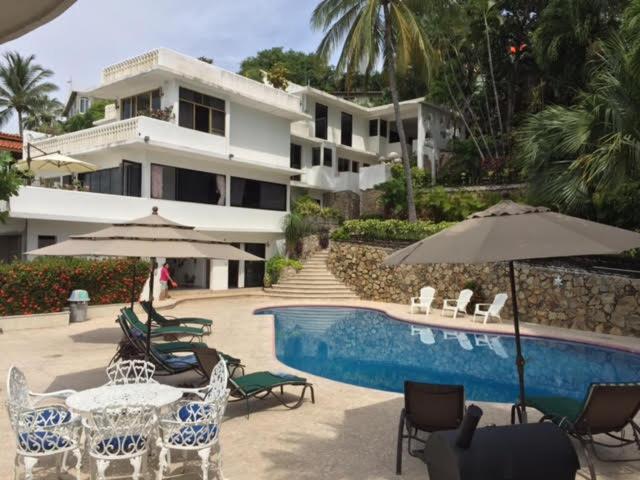 una piscina con sillas y sombrillas frente a una casa en Gran habitacion con terraza vista espectacular, piscina en Acapulco