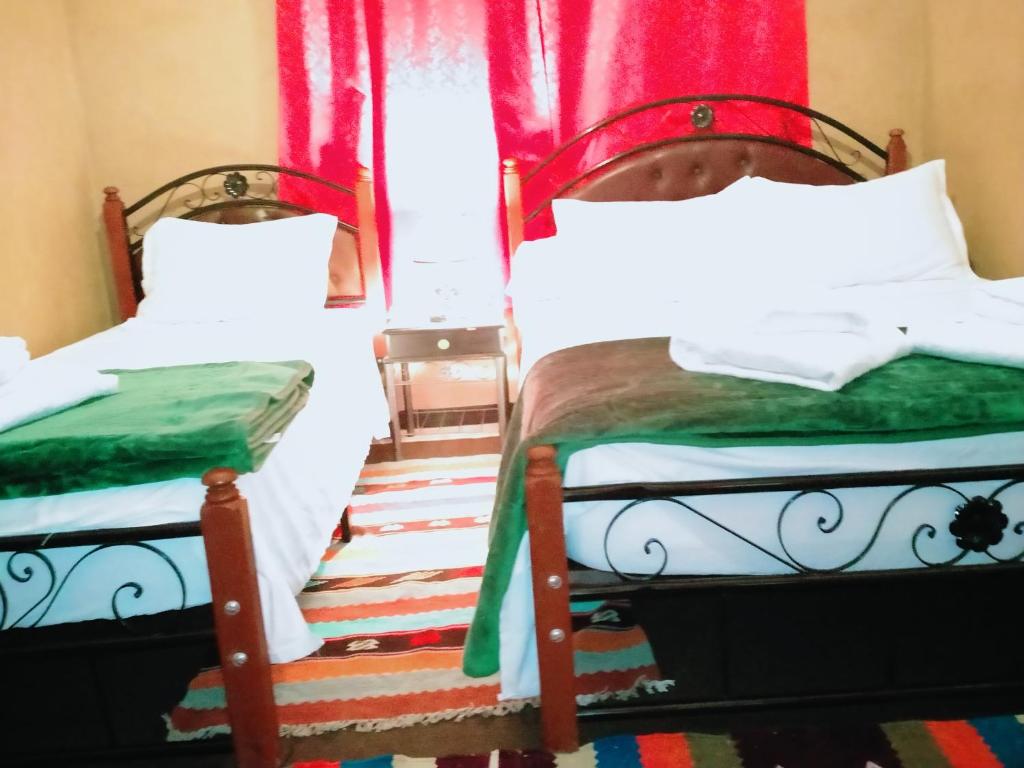 deux lits jumeaux dans une chambre avec des rideaux rouges dans l'établissement Maison d'Hôtes Ghalil, à Ouarzazate