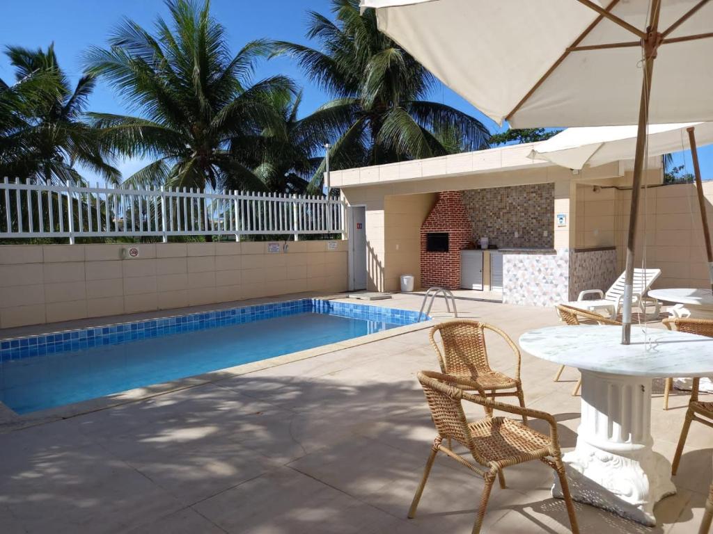 einen Pool mit Stühlen, einem Tisch und einem Sonnenschirm in der Unterkunft Village - Condomínio Mansão da Lagoa in Salvador