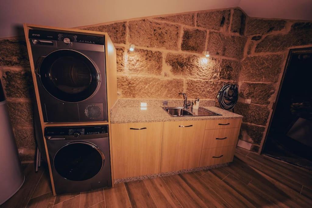 a kitchen with a washer and a sink and a stone wall at Casa Rural Vilar de Flores in Ourense
