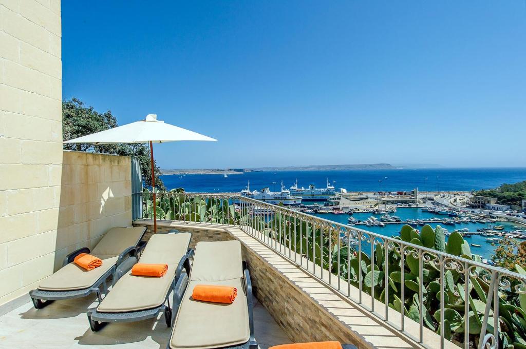 a balcony with chaise lounge chairs and an umbrella at The Harbour Holiday Home in Għajnsielem