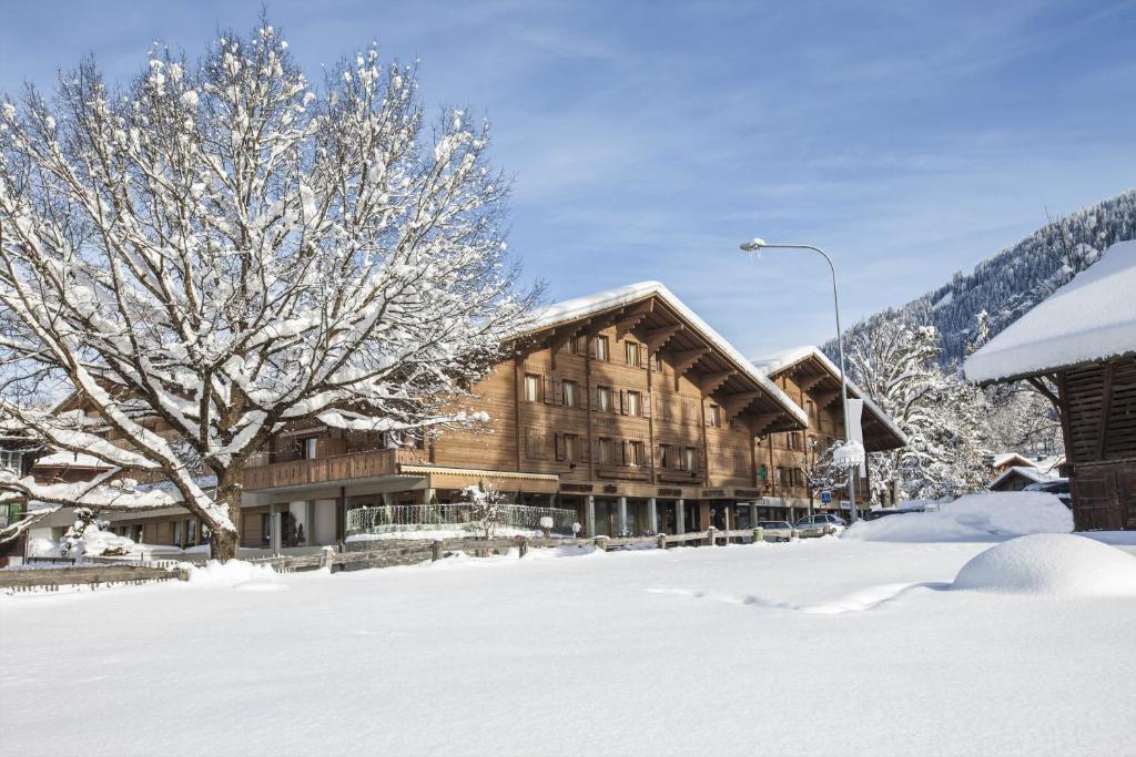 a large wooden building in the snow with a tree at Gstaaderhof - Active & Relax Hotel in Gstaad